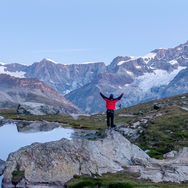 Mann steht in den Bergen vor dem Matterhorn und hält die Hände in die höhe.